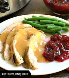 a white plate topped with meat covered in gravy next to green beans and cranberry sauce