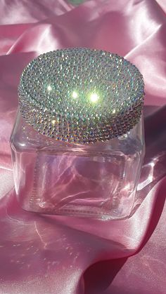 a close up of a glass container on a pink satin surface with a diamond covered lid