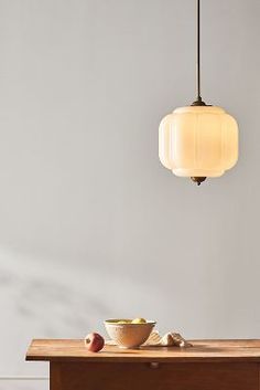 a wooden table topped with a bowl of fruit next to a light hanging over it