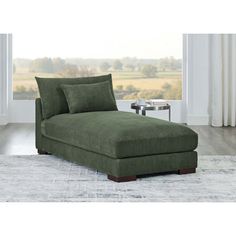 a large green chaise lounger in front of a window with a rug on the floor