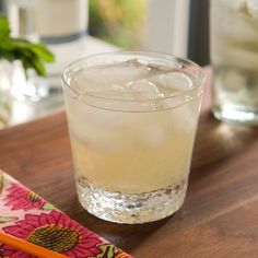 a glass filled with ice sitting on top of a wooden table next to a pencil