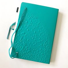 a green notebook covered in water droplets on a white surface with a blue ribbon attached to the cover