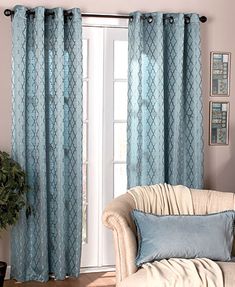 a living room with a couch, chair and window covered in blue curtain panels next to a potted plant