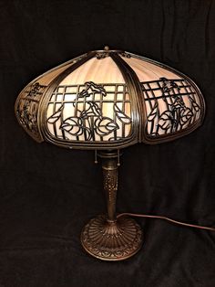 a lamp that is sitting on top of a black cloth covered tablecloth with an intricately designed glass shade