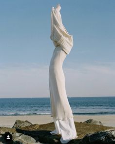 a woman is standing on the beach with her arms in the air and looking at the ocean