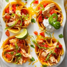 several tacos with chicken, peppers and sour cream on a white platter next to lime wedges