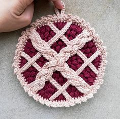 a hand holding a crocheted dishcloth in the shape of a circle on concrete