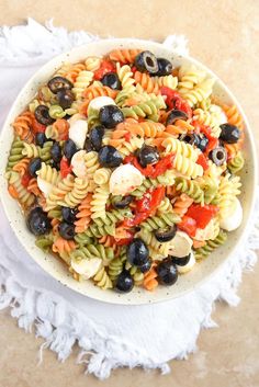 a bowl filled with pasta and olives on top of a white cloth next to a fork