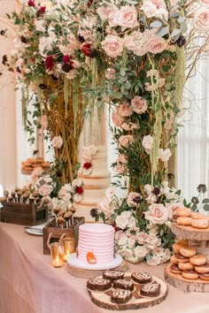 a table topped with cakes and donuts next to tall vases filled with flowers