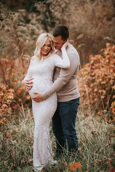 a pregnant couple cuddles in the middle of a field with tall grass and orange flowers