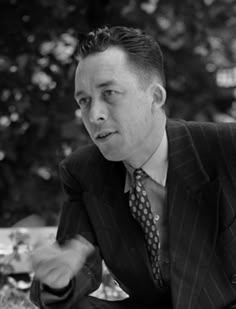 a man in a suit and tie sitting on a bench with his hand out to the side