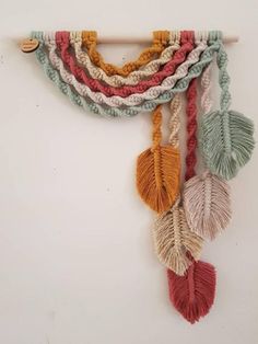 a multicolored wall hanging with tassels and leaves on the side, attached to a white wall