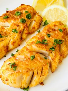 two pieces of chicken on a white plate with lemon wedges and parsley garnish