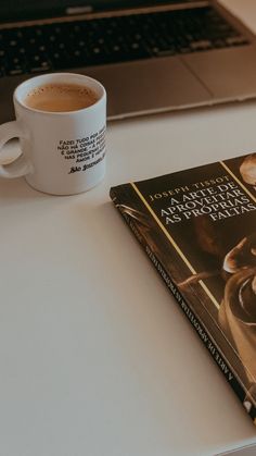 a coffee cup sitting on top of a book next to a laptop