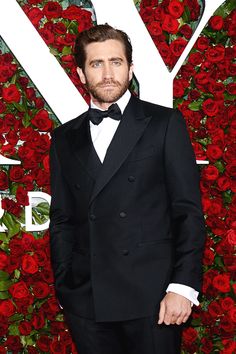 a man in a tuxedo and bow tie standing on a red carpet with roses