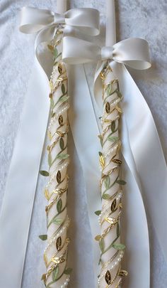 two white ribbons with gold leaves and pearls tied to them on top of a bed