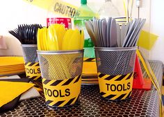 there are two cups that have tools in them on the table with yellow and black tape