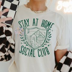 a woman wearing a white t - shirt with the words stay at home social club on it