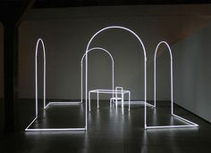 an illuminated room with arches and tables on the floor, in front of a white wall