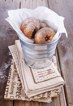 powdered doughnuts in a metal bowl on napkins next to a wooden table