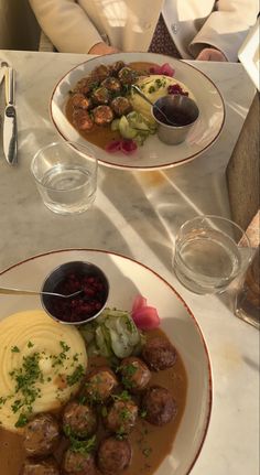 two plates filled with meatballs, mashed potatoes and gravy on a table