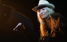 a woman with long hair wearing a hat and holding a microphone in front of her