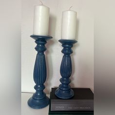 two blue candles sitting on top of each other next to a book and a white wall