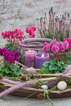 purple flowers and candles are arranged in a wicker basket on a table with lavenders