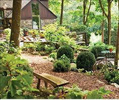 an outdoor area with benches, bushes and trees in the foreground is a house