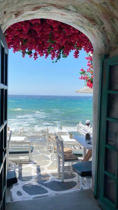 an open door leading to the beach with flowers hanging from it's roof and ocean in the background