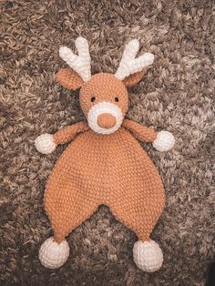 a knitted stuffed animal laying on top of a carpet covered in brown and white yarn