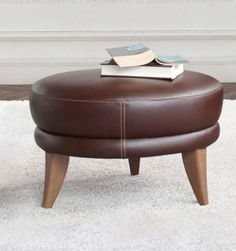 a brown ottoman sitting on top of a white rug next to a table with a book on it