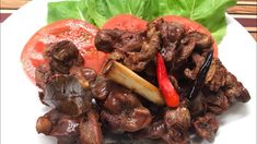 a white plate topped with meat and veggies next to lettuce leaves