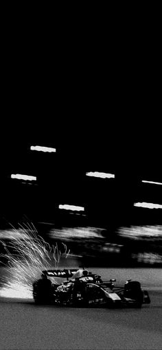 a black and white photo of a racing car speeding down the track at night time