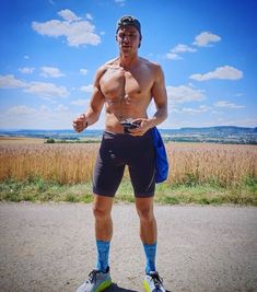 a shirtless man standing on a skateboard in front of a wheat field and blue sky