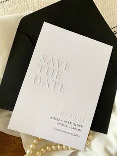 an elegant save the date card on top of some black and white envelopes with pearls