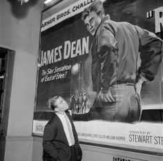 a man standing in front of a large poster on the wall next to a book shelf