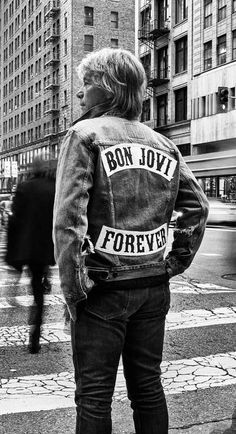 a man standing on the street with his back to the camera, wearing a jean jacket that says bon jovi forever