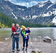 a man, woman and two children standing in front of a mountain lake