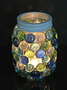 a jar filled with lots of different colored glass beads on top of a black table