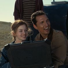 a man and woman sitting in the back of a truck holding a black piece of luggage