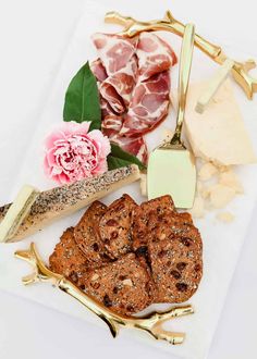 an assortment of meats and cheeses on a plate with gold utensils