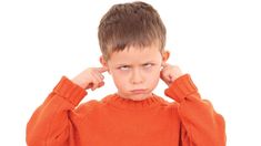 a young boy in an orange sweater holding his hands to his ears