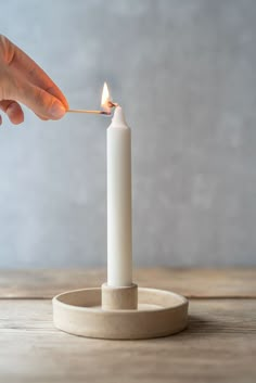 a person lighting a candle with a match stick in their hand on a wooden table