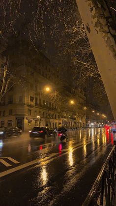 cars driving down the street at night on a rainy day with buildings in the background