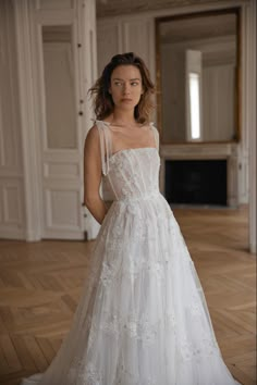 a woman in a white wedding dress standing on a wooden floor with her hands on her hips