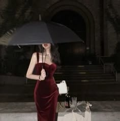 a woman in a red velvet dress holding an umbrella over her head while standing on the sidewalk