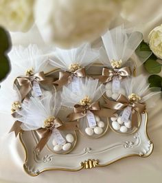 three white and gold wedding favors in a tray with flowers on the side, along with two roses