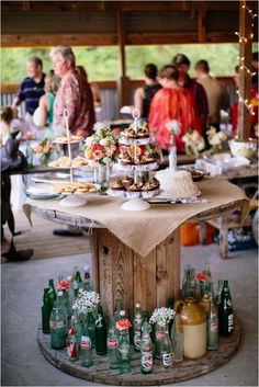 a wooden table topped with lots of food and drinks next to people standing in the background