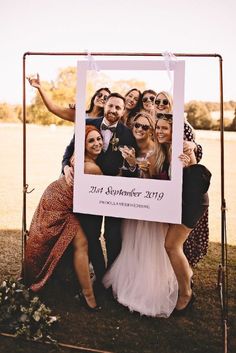 a group of people standing next to each other in front of a photo frame on a metal stand